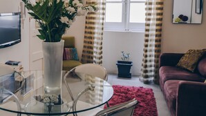 Un salon moderne avec une table à manger en verre, un canapé, un téléviseur et une fenêtre avec des rideaux.