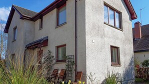 Een woonhuis met twee verdiepingen, een schuin dak, meerdere ramen en een schoorsteen.