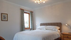 Een netjes opgemaakt bed met witte lakens, een houten nachtkastje met een lamp en een raam met gordijnen.