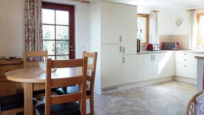 Een keuken met witte kastjes, een houten eettafel en stoelen.