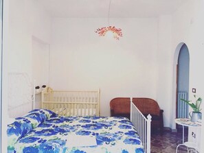 A bedroom with a bed, a crib, a chair, and a small table with a plant.