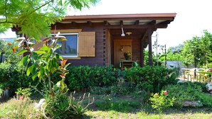 A wooden cabin with a large window and a door, surrounded by a well-maintained garden with various plants and a small table with chairs. - B&B SanteBice (Polignano a Mare)