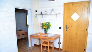 A room with a wooden table, a chair, a wooden door, and a small shelf with figurines. - B&B SanteBice (Polignano a Mare)