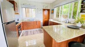 Een moderne keuken met granieten werkbladen, houten keukenkastjes, een roestvrijstalen koelkast en een groot raam voor natuurlijk licht.