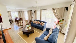 Een ruime woonkamer met een blauwe bank, een eethoek met stoelen en een televisie.