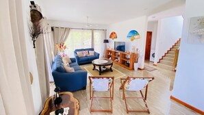 Een ruime woonkamer met een blauwe bank, een bijzettafeltje en een tv-meubel. Er is een trap die naar een ander niveau leidt.