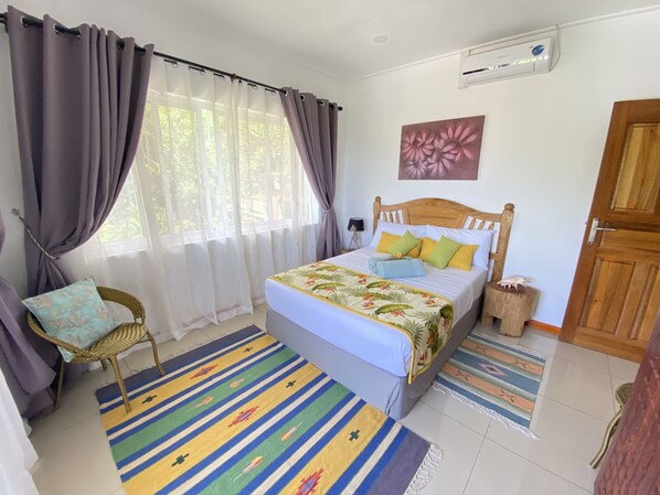 Un dormitorio con cama, cortinas, una silla, un tapete y una puerta de madera.