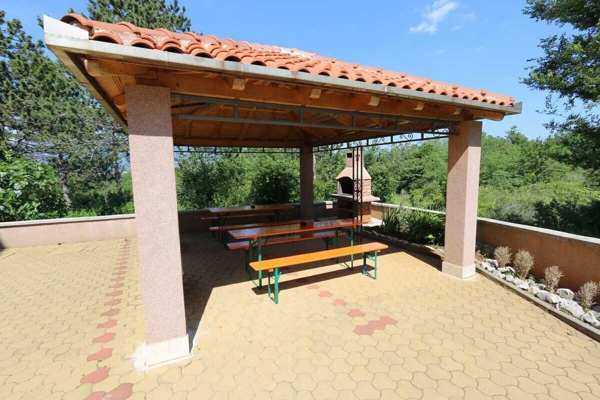 An outdoor pavilion with a tiled roof, benches, and a brick oven.