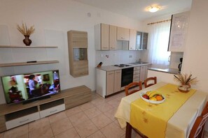 Une cuisine compacte avec un coin repas, un téléviseur posé sur un meuble et une table sur laquelle se trouve un panier de fruits.