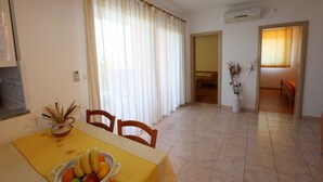 Un coin repas avec une table dressée pour deux personnes, un vase contenant des plantes séchées et une vue sur une chambre à coucher.