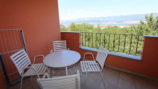 Un balcon avec une table ronde et des chaises blanches, d’où l’on peut admirer un paysage lointain.