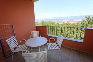 Un balcon avec une table ronde et des chaises blanches, d’où l’on peut admirer un paysage lointain.