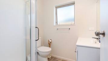 A modern bathroom with a glass shower enclosure, a toilet, a window, and a sink.