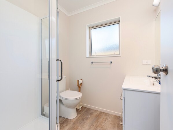 A modern bathroom with a glass shower enclosure, a toilet, a window, and a sink.