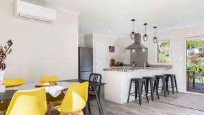 A modern kitchen with a central island, black bar stools, and a dining area with yellow chairs.