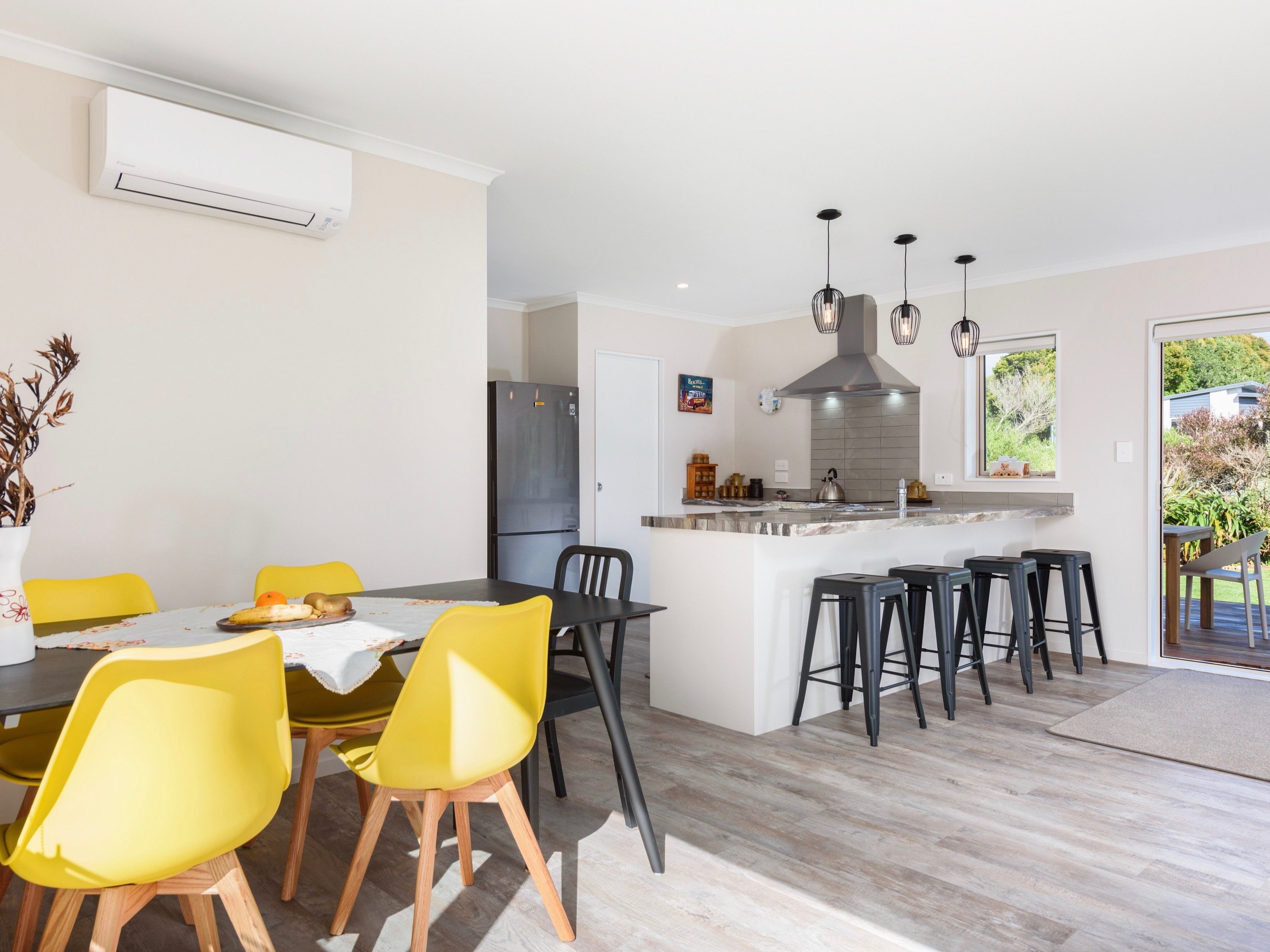 Una cocina moderna con una isla central, taburetes negros y un área de comedor con sillas amarillas.