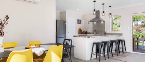 A modern kitchen with a central island, black bar stools, and a dining area with yellow chairs.