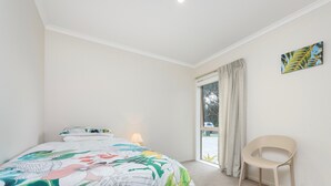 A bedroom with a bed, a chair, a window with curtains, and a painting on the wall.