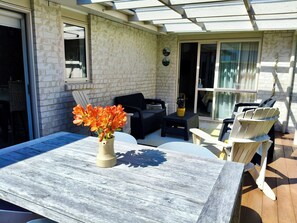 Un patio al aire libre con mesa de madera, sillas y un jarrón de flores.