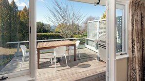 Une terrasse en bois avec une table et des chaises, un barbecue et une vue sur les arbres et les bâtiments.