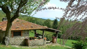 Un edificio rústico de piedra con tejado de baldosas, un porche de madera y plantas en macetas.
