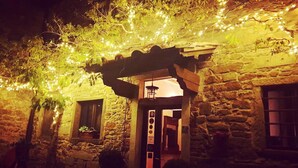 Un edificio de piedra con un arco de entrada de madera, hiedra y luces colgantes.