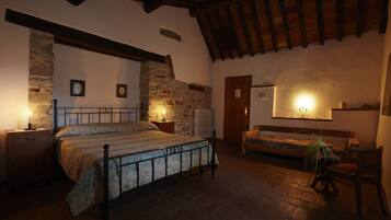 A bedroom with a bed, wooden beams, stone walls, a bench, and a chair.