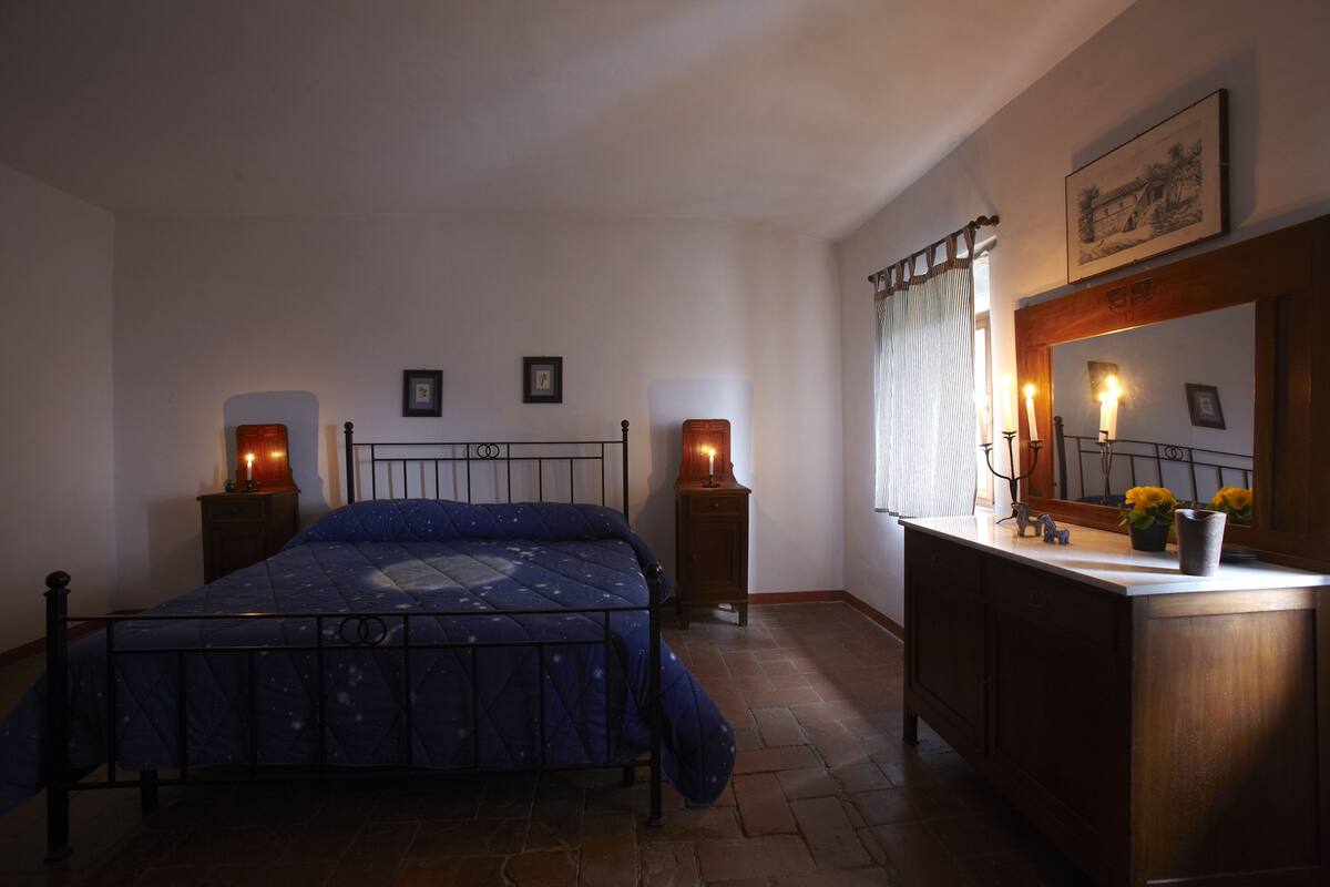 Un dormitorio con cama, lámparas de noche, cómoda, espejo y un cuadro en la pared.
