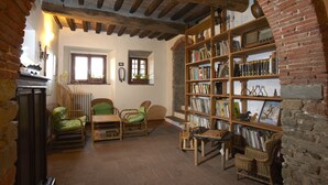 Una habitación acogedora con vigas de madera a la vista, una estantería llena de libros y objetos decorativos, muebles de mimbre y una chimenea.
