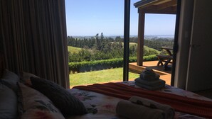 A bedroom with a large bed, a view of a garden and hills, and a wooden deck outside.