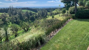 A lush green landscape with a clear view of distant hills and a body of water under a blue sky.
