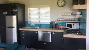 A modern kitchen with a stainless steel refrigerator, a microwave, a stove, and a sink. There is a window with blinds, a clock on the wall, and a vase with flowers on the counter.