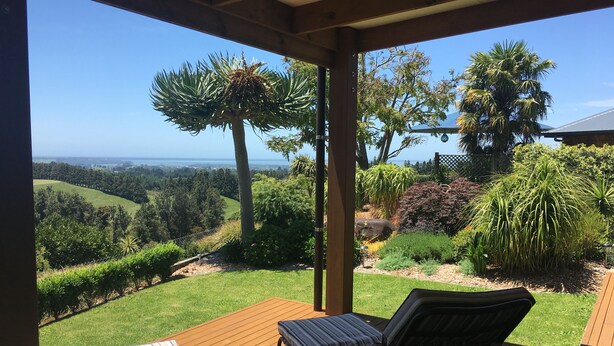 A covered outdoor seating area with a view of a landscaped garden and distant landscape.