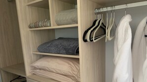 A wooden closet with shelves, a hanging rack, and a robe hanging on the right.