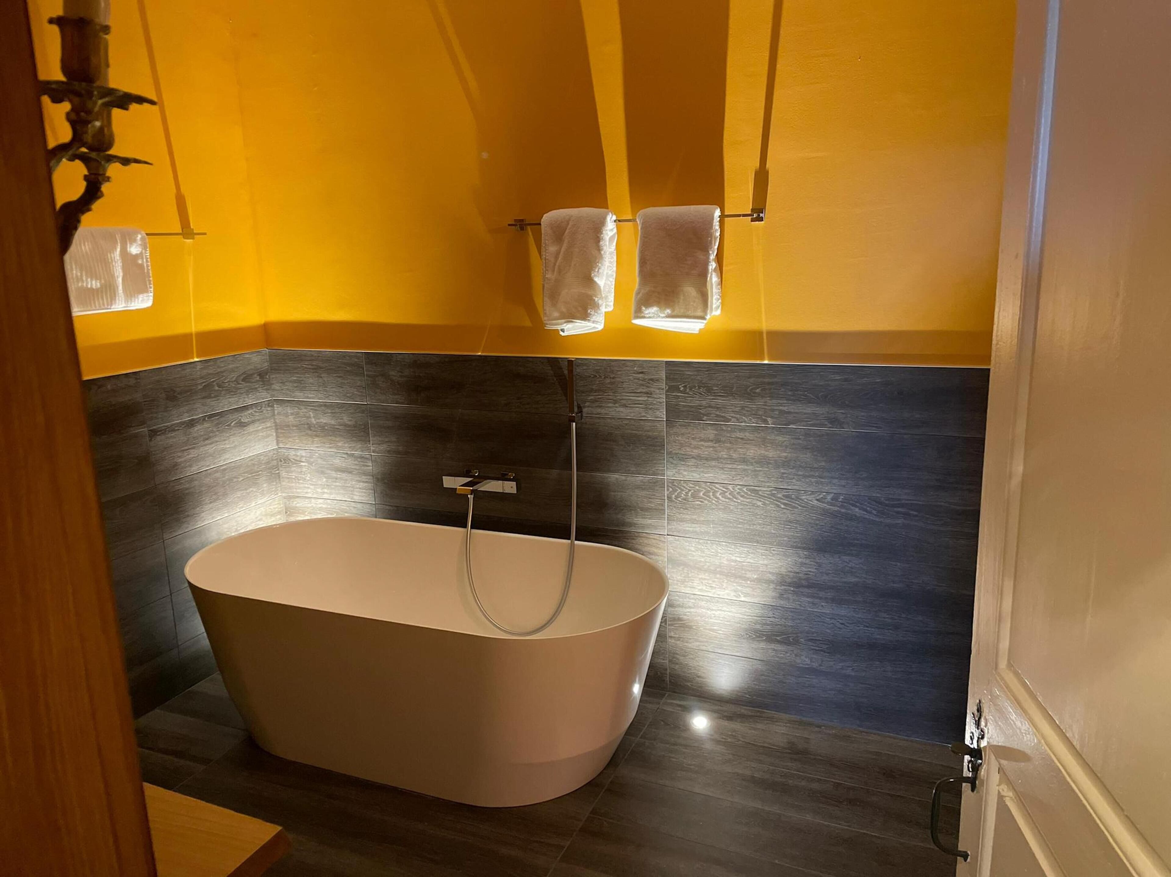 A modern bathroom with a freestanding bathtub, dark tiled walls, and a yellow accent wall.