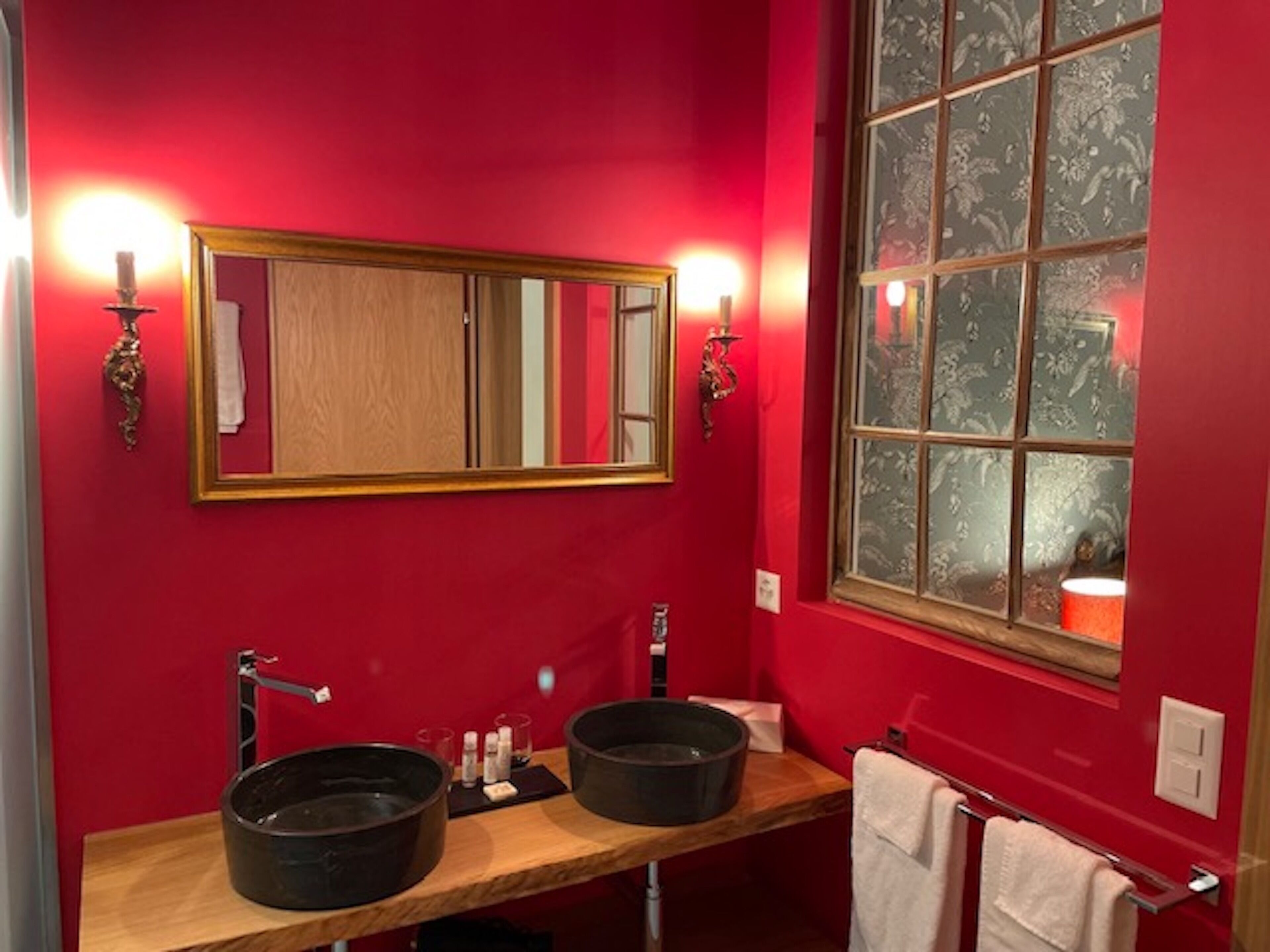 Une salle de bain avec deux lavabos, un grand miroir et une fenêtre agrémentée de rideaux à motifs floraux.
