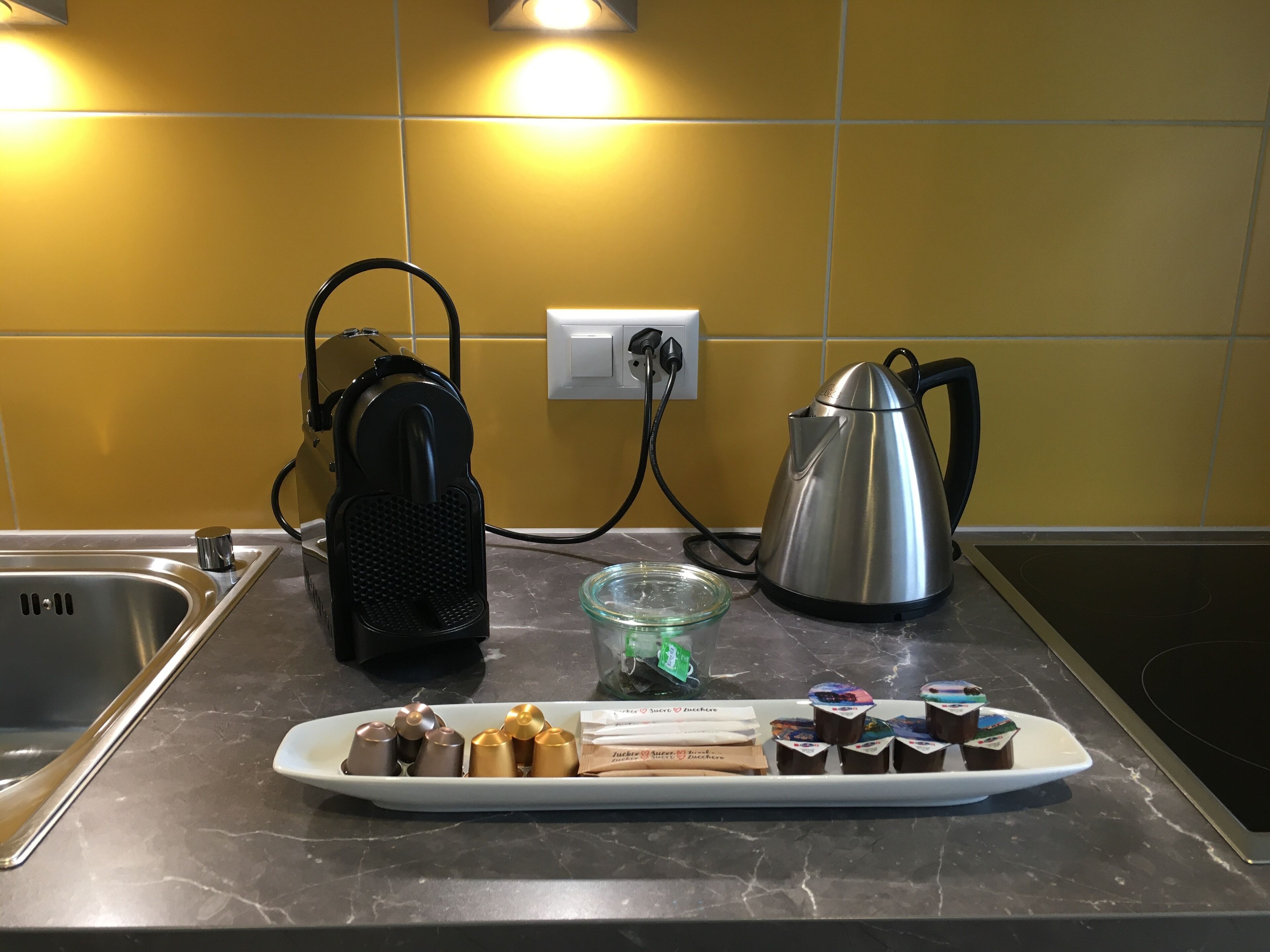 A kitchen counter with a coffee maker, kettle, and a plate of pastries.