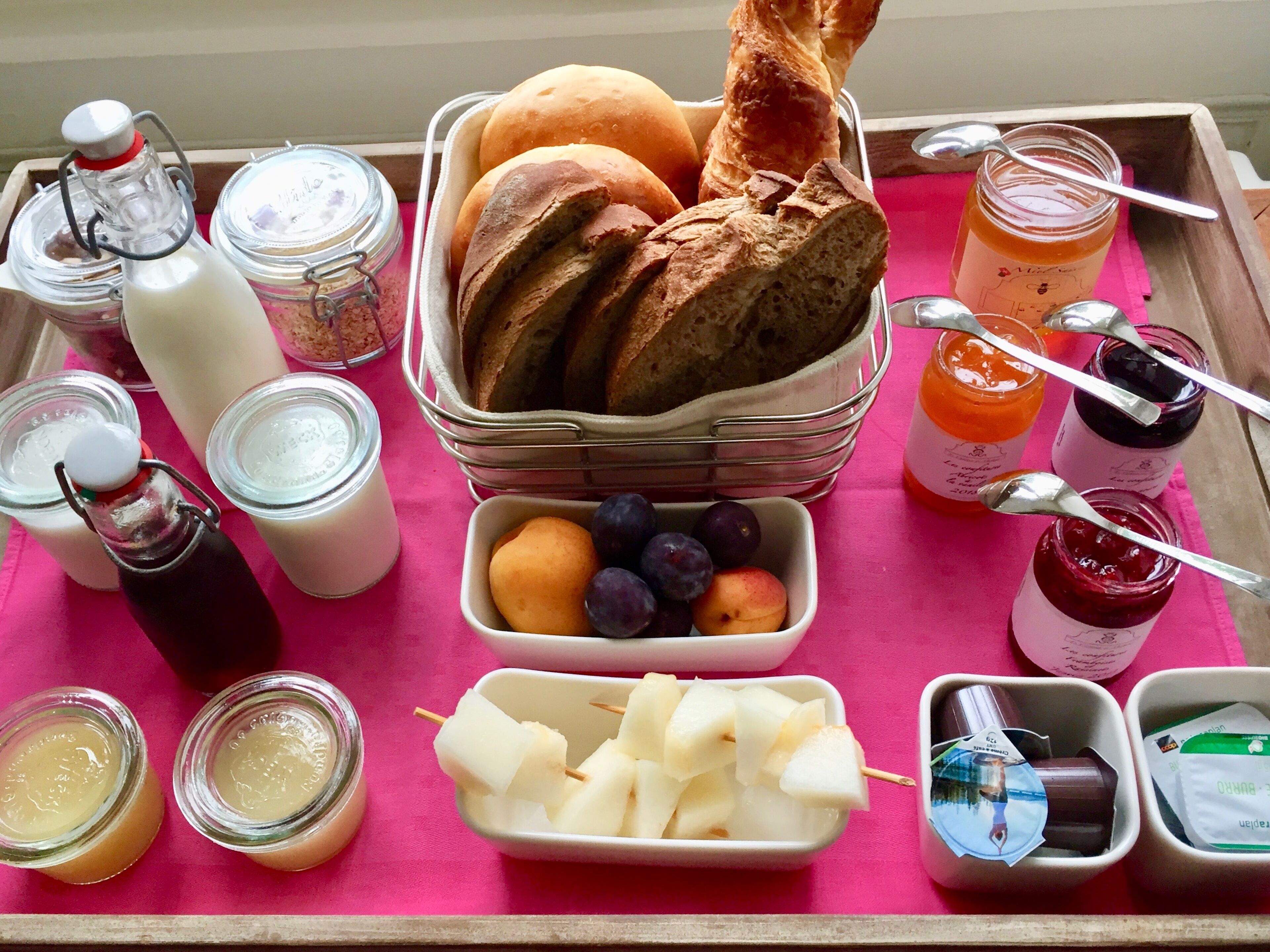 Un plateau avec du pain, des fruits et des pots de confitures.