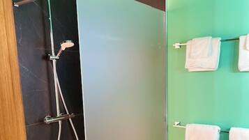 A bathroom with a shower, a towel rack with towels, and a door.