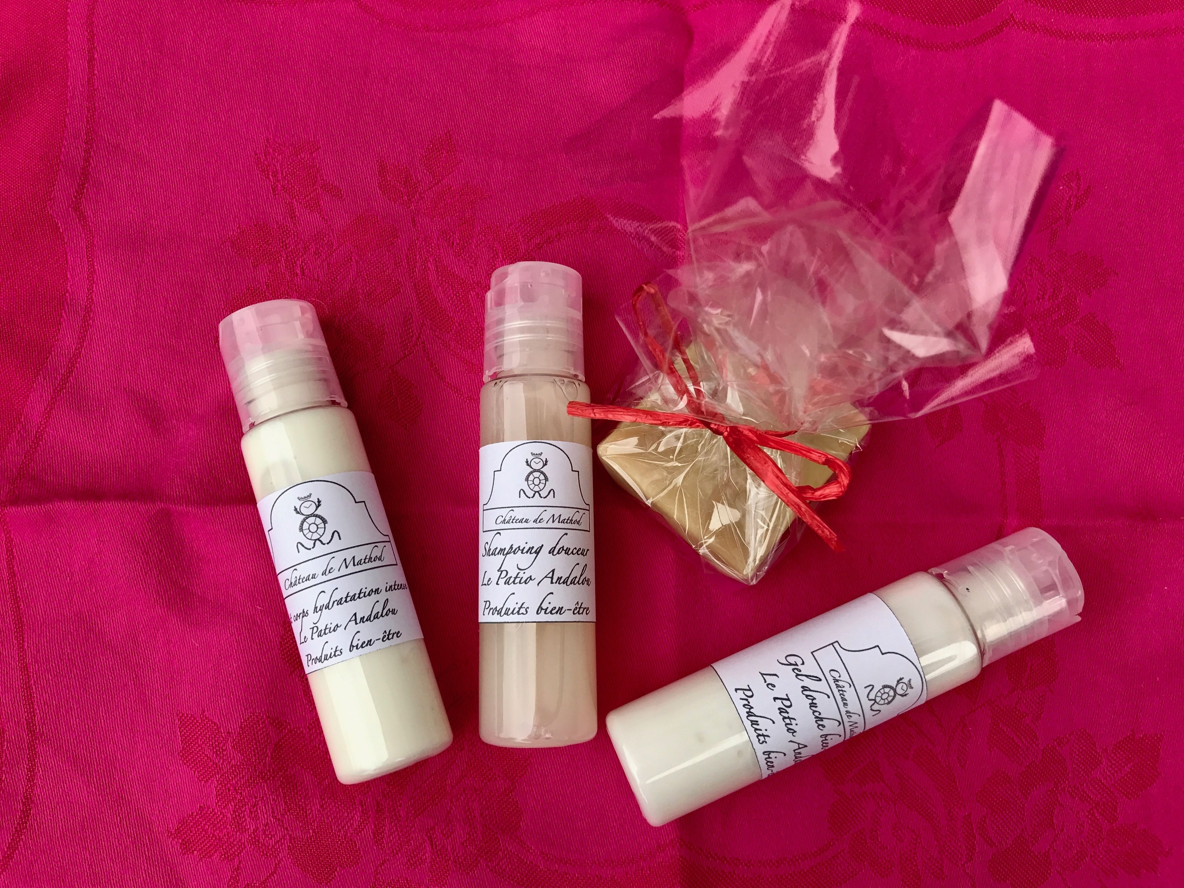Vier flesjes lotion en een klein cadeautje op een roze doek.