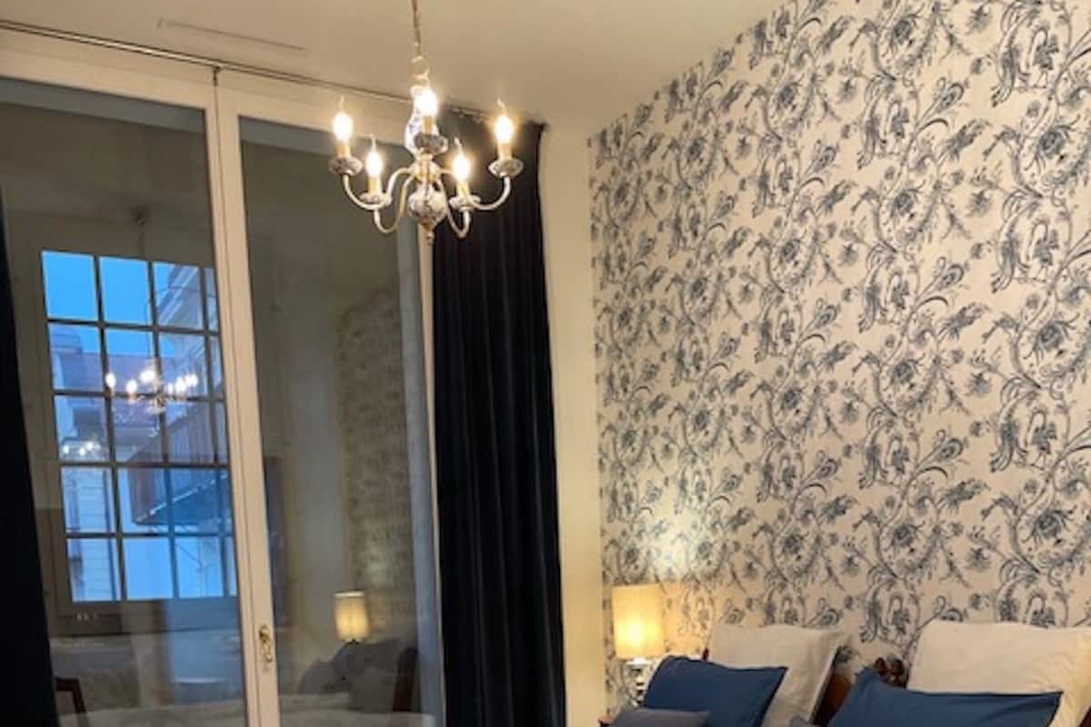 Ein Schlafzimmer mit einem großen Bett, einem hölzernen Nachttisch, einer Chandelüster und einer Wand mit Muster.