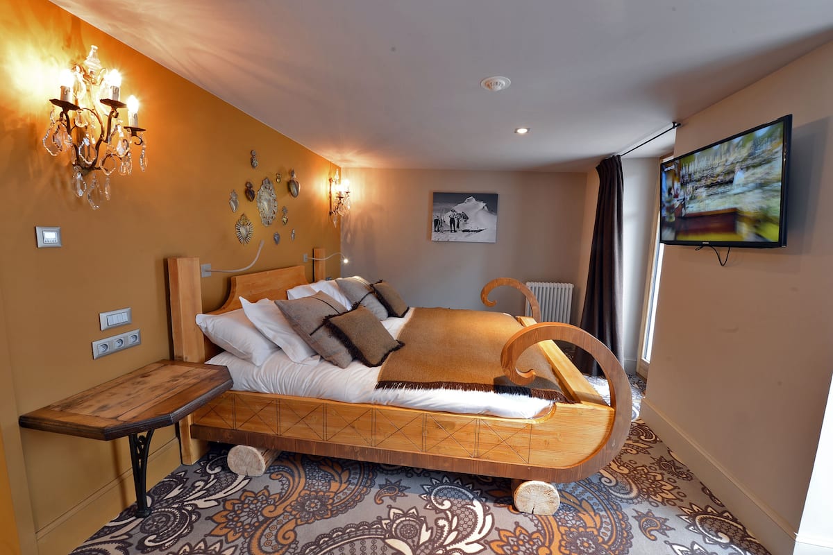 Une chambre à coucher dotée d’un lit au design incurvé original, d’un lustre, d’un téléviseur fixé au mur et d’une moquette à motifs.