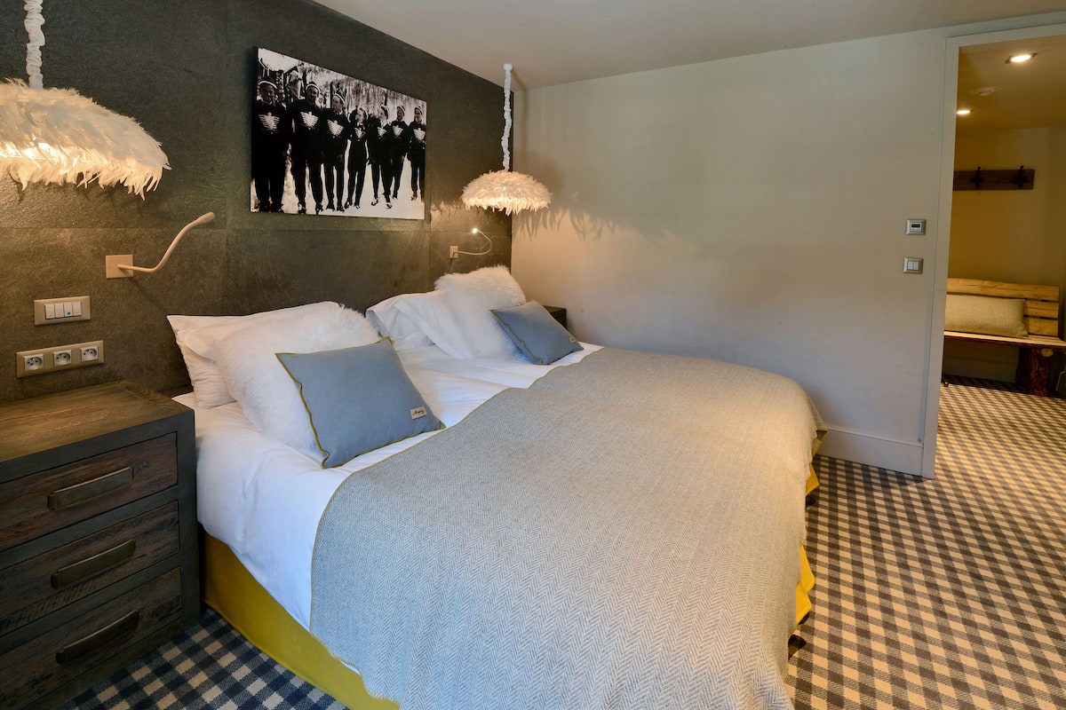 Une chambre à coucher avec un lit, une table de chevet, une lampe fixée au mur et un sol à carreaux.