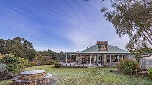 Une maison de campagne avec une véranda couverte, une terrasse en bois et une table de pique-nique dans le jardin.