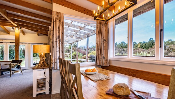 Un coin repas rustique, avec des meubles en bois, un lustre et de grandes fenêtres donnant sur l’extérieur.
