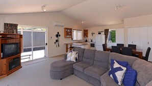 Ein geräumiger Wohnbereich mit grauem Ecksofa, einer Holz-Unterhaltungseinheit und einer Küchenzeile mit Kühlschrank und Mikrowelle.