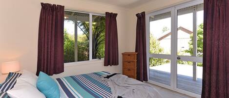 Una camera da letto con un letto, un comodino, una lampada, una finestra con tende e vista su del verde all'esterno.