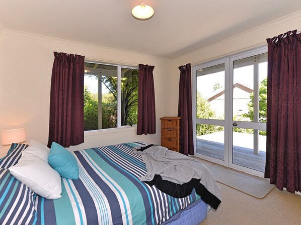A bedroom with a bed, a nightstand, a lamp, a window with curtains, and a view of greenery outside.