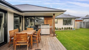 Ein moderner Außenküchenbereich mit Holztisch und -stühlen, einem Grill und einer überdachten Terrasse.
