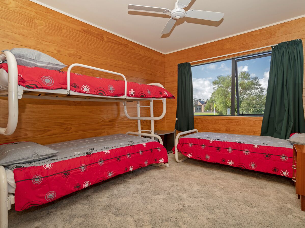 Une chambre avec des lits superposés, un ventilateur de plafond, une fenêtre avec des rideaux et une vue sur les arbres.